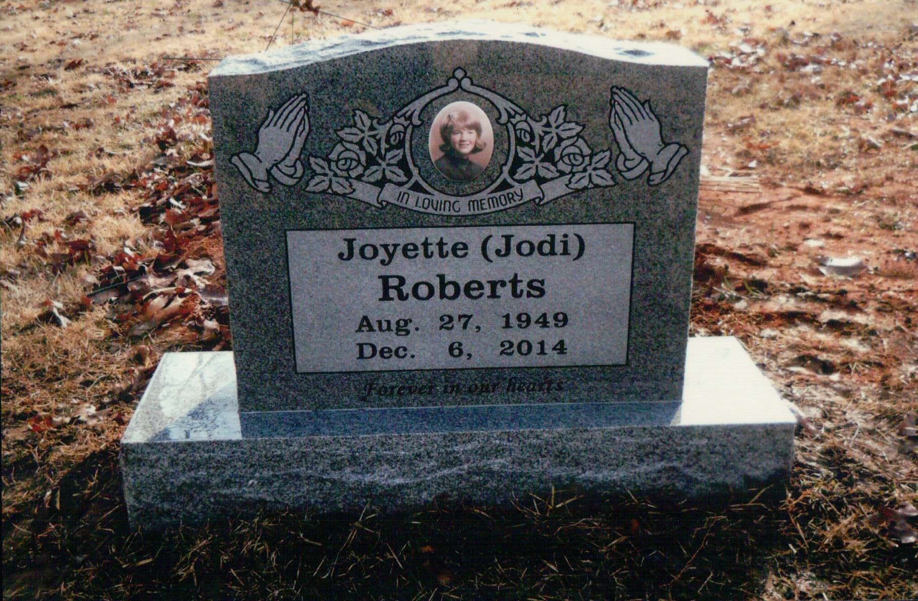 A gravestone for Joyette (Jodi) Roberts, inscribed with dates Aug. 27, 1949 – Dec. 6, 2014, with portrait and praying hands.