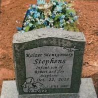 A gravestone for Kaizer Montgomery Stephens, dated Oct. 22, 2018, with floral arrangements on top.