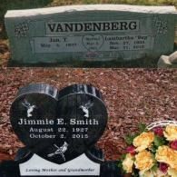 A gray stone Vandenberg family monument positioned behind a black heart-shaped headstone for Jimmie E. Smith with flowers.