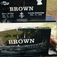 A black granite double headstone for the Brown family, featuring names, dates, a cross, and an engraved train image.