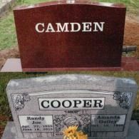 Two grave markers in a grassy cemetery: a red stone with 
