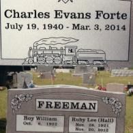 Two headstones in a cemetery: one for Charles Evans Forte (1940-2014) with a train carving, the other for the Freeman family.