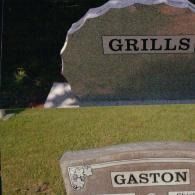 Two gray stone grave markers stand in a green grassy cemetery, with 