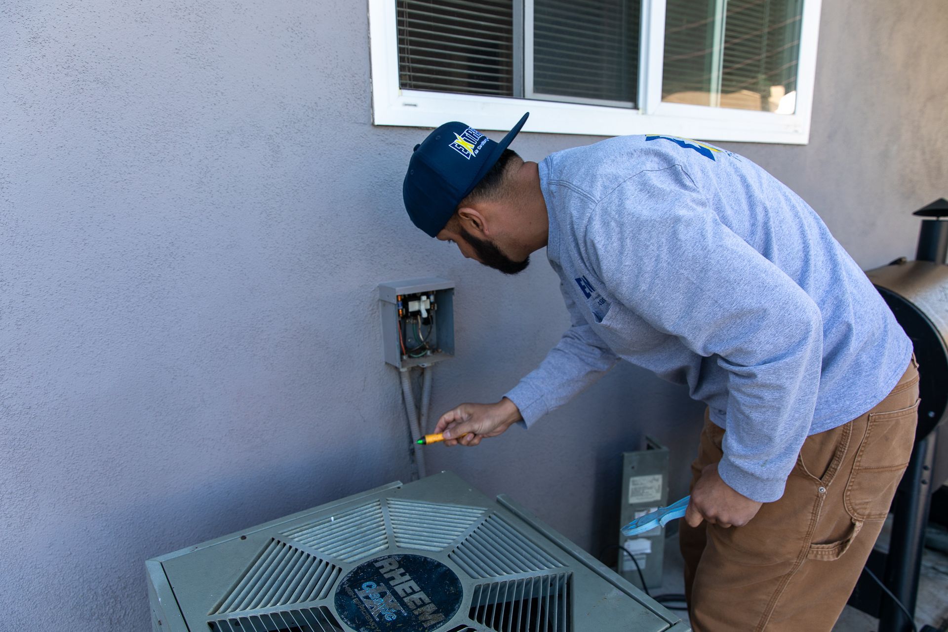 A man wearing a hat with a star on it is working on an air conditioner