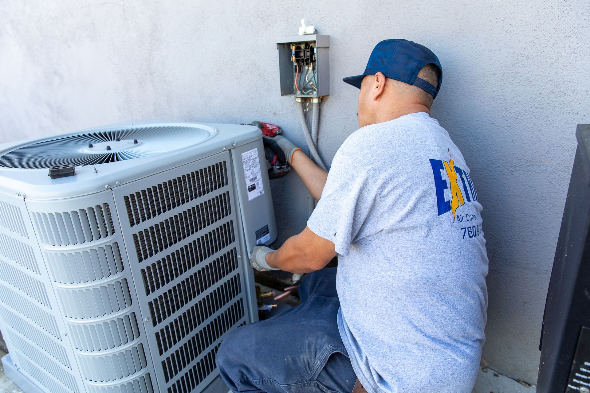 A man wearing a gray shirt with the letter n on it is working on an air conditioner