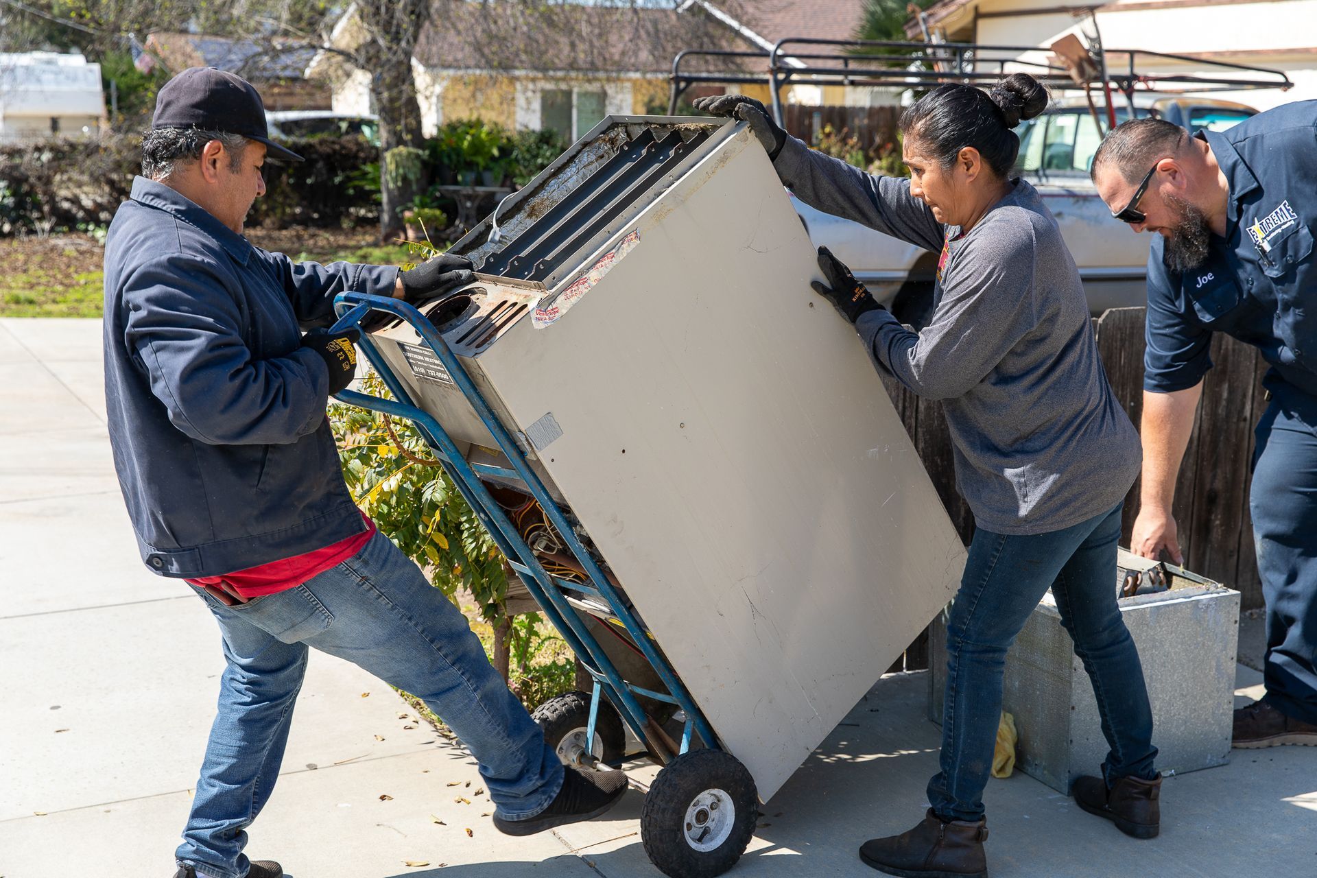 A group of people are pushing a refrigerator on a dolly