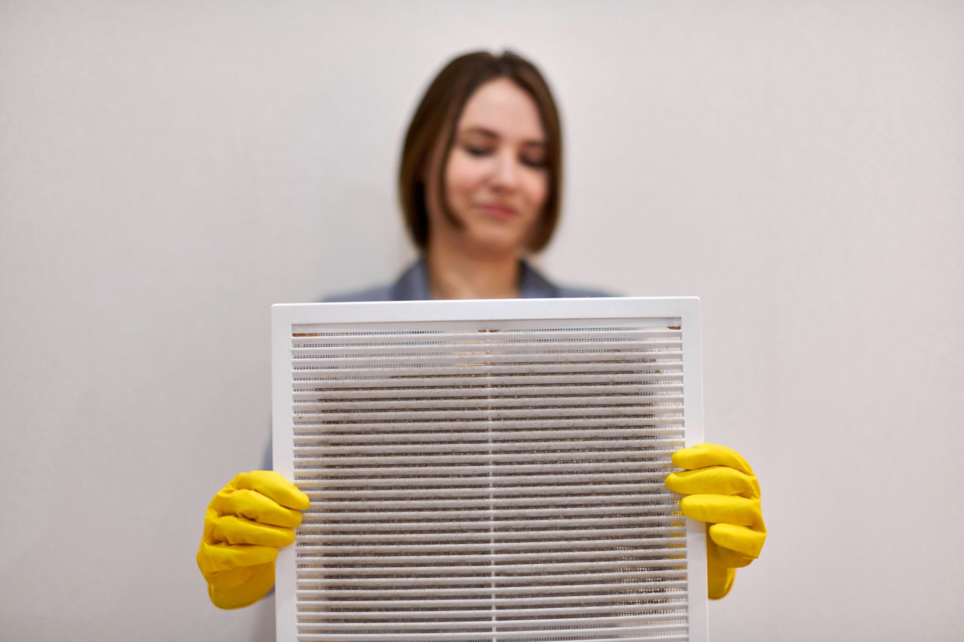 A woman wearing yellow gloves is holding a dirty air filter.