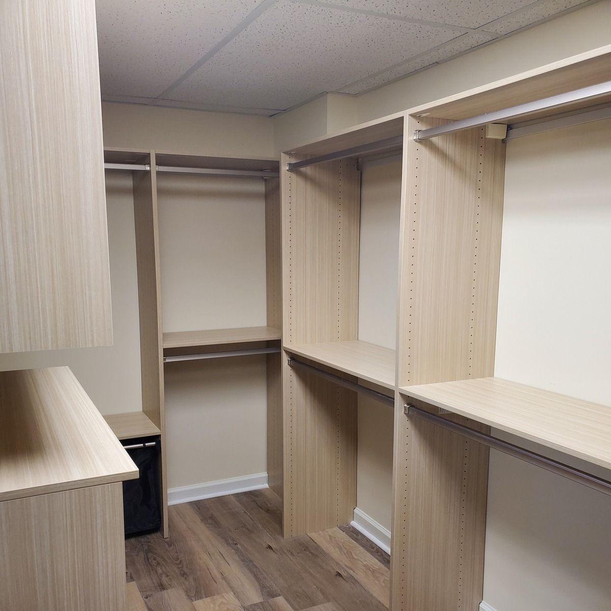 A walk-in closet with wooden shelves and hanging rods.  It has light-colored wood accents, with a black item near the corner.