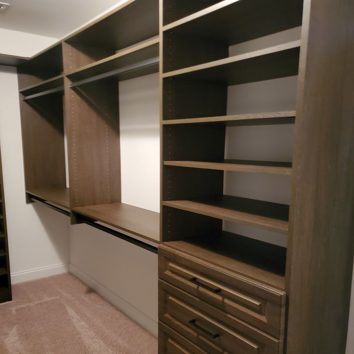 Custom walk-in closet with dark brown shelving, drawers, and hanging rods. Beige carpet and white walls.