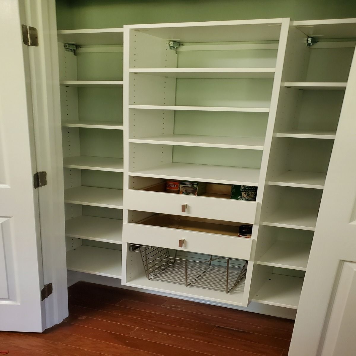 White closet shelves and drawers built into a closet, with a wire basket.