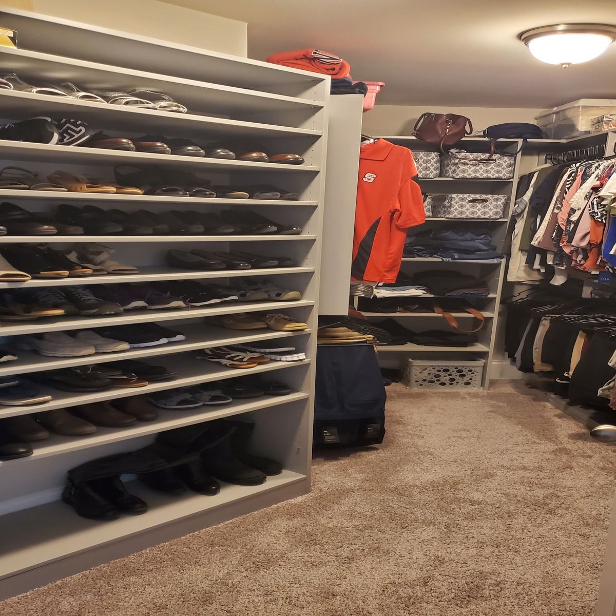 A walk-in closet filled with shoes, clothes, and shelving, organized with a neutral carpet.
