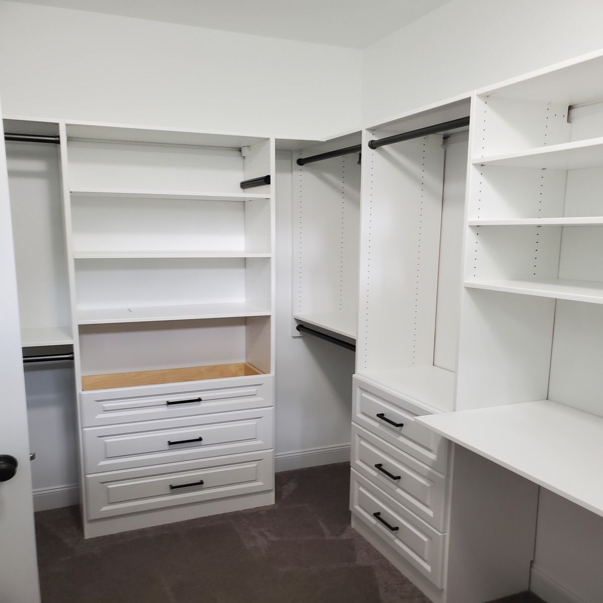 White, custom-built closet with shelves, drawers, and hanging rods. It's empty, ready for clothes, with a built-in desk on the right.