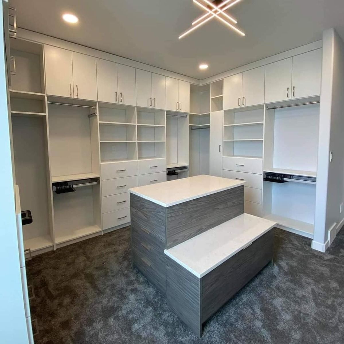 Spacious, white walk-in closet with a gray island, shelving, and cabinets. Modern design, neutral color palette.