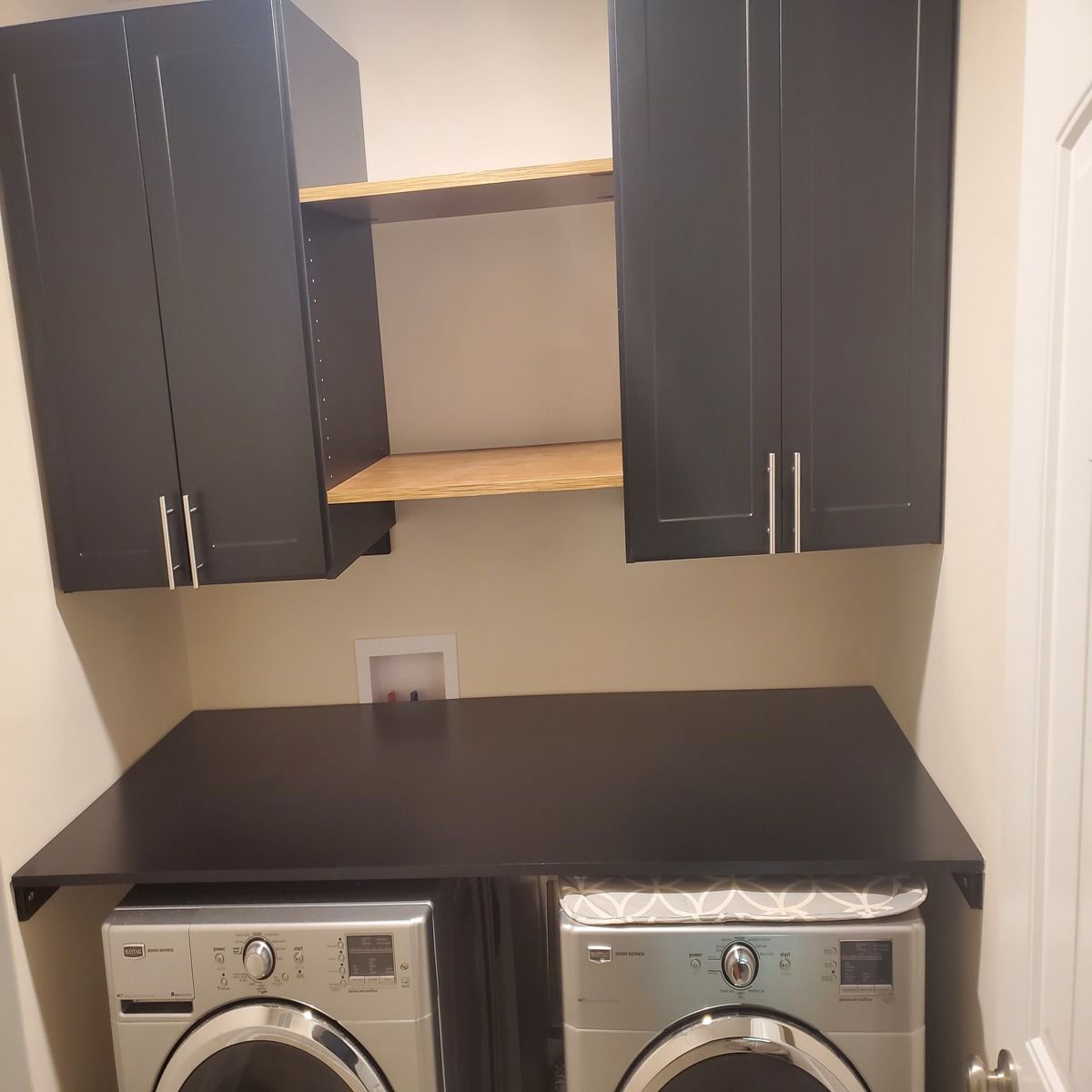 Laundry room with black cabinets and countertop over a washer and dryer; a shelf sits between the cabinets.
