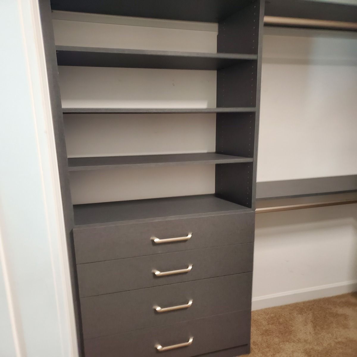 Dark gray closet organizer with shelves and drawers, placed in a closet with a hanging rod.