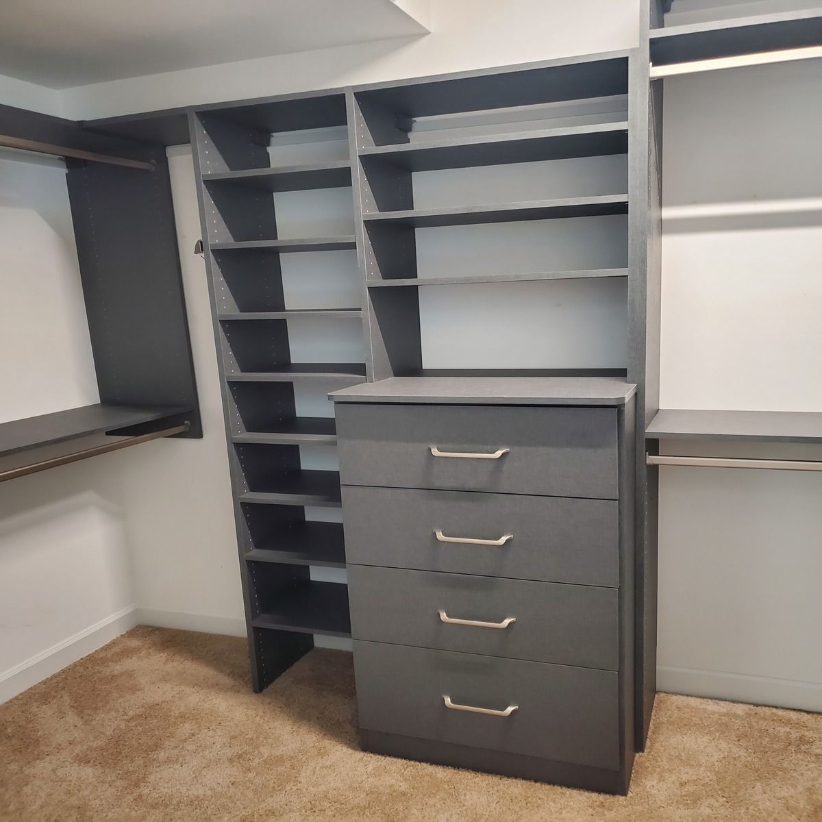 Dark gray closet organization system with shelves and drawers. The system is placed inside a white-walled closet with beige carpet.