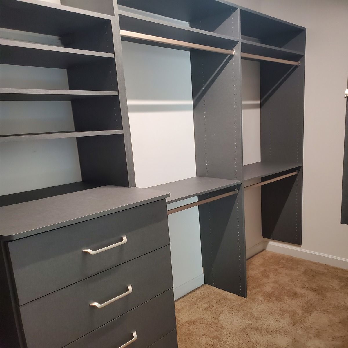 Dark gray custom closet organization system with shelves, drawers, and rods. The carpet is beige.