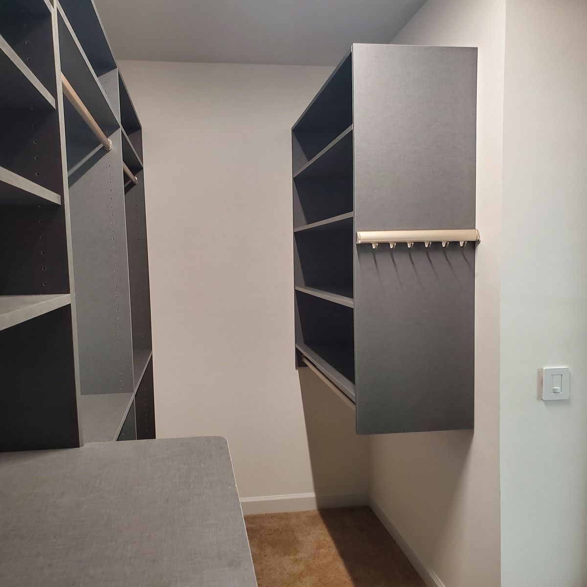 Walk-in closet with dark gray shelving and a hanging rod. Light tan carpet and beige walls.