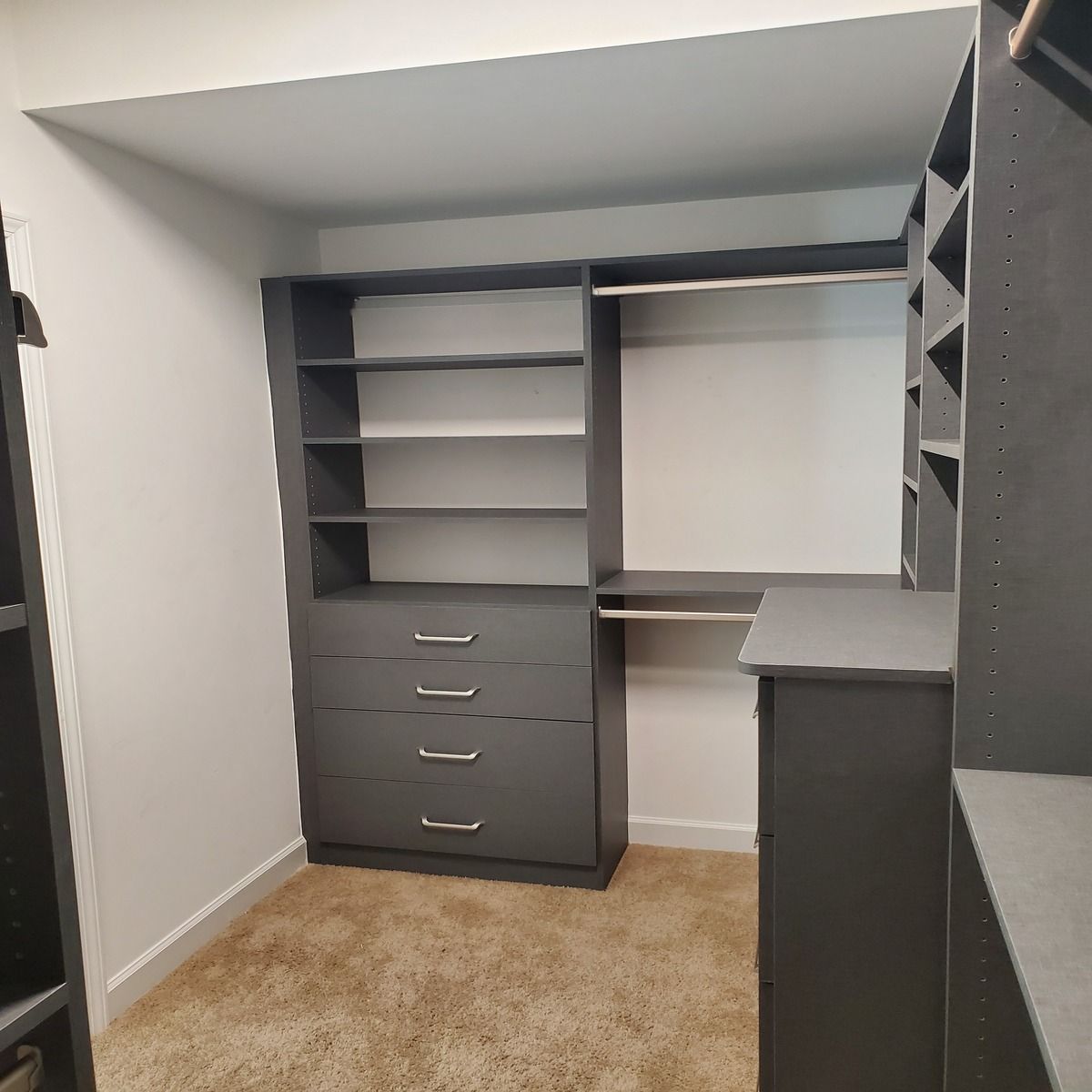 A walk-in closet with gray shelving, drawers, and hanging rods; carpeted floor and white walls.