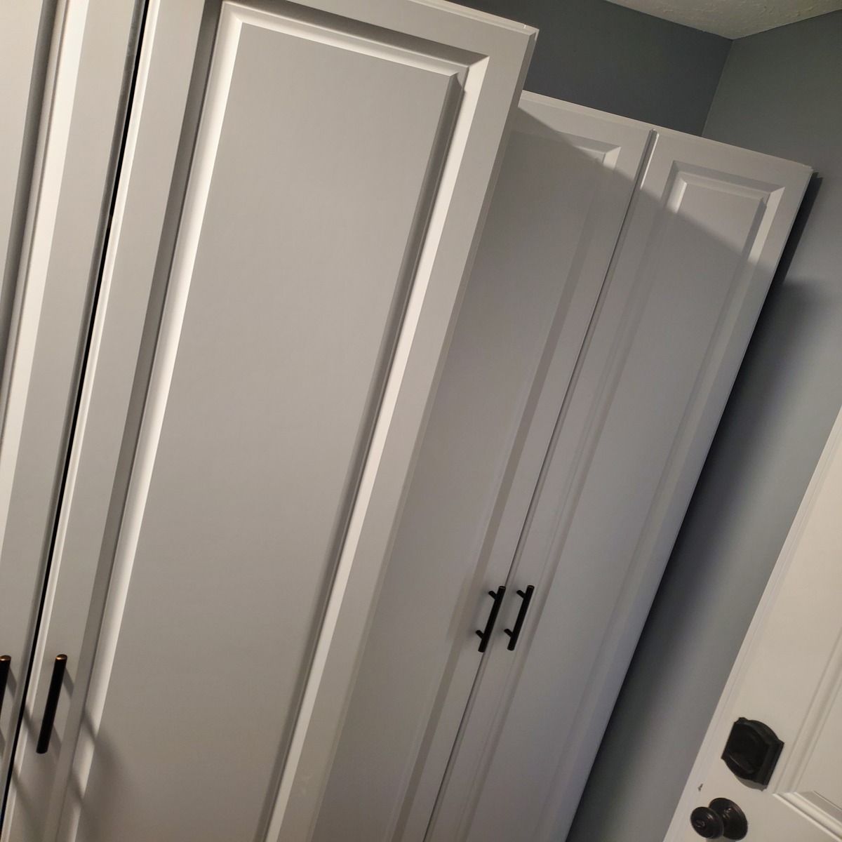 White storage cabinets against a light blue wall. The cabinets have black handles.