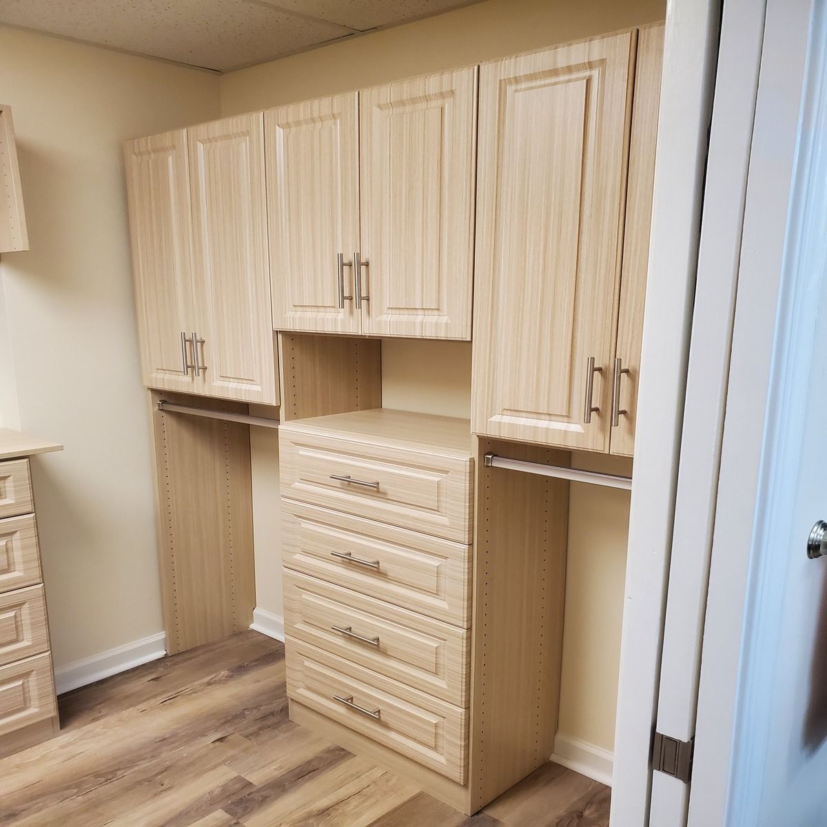 Beige wooden cabinets with drawers and hanging rods in a room with wooden floors and a white door.