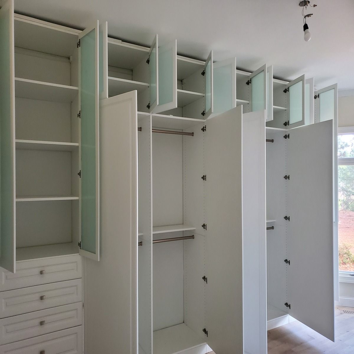 White, open closet with multiple shelves, drawers, and hanging rods. Frosted glass doors and cabinet doors are open.