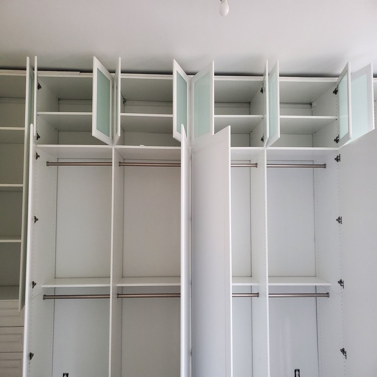 White closet with multiple sections, open doors, and shelves. Hanging rods and frosted glass upper door panels are visible.