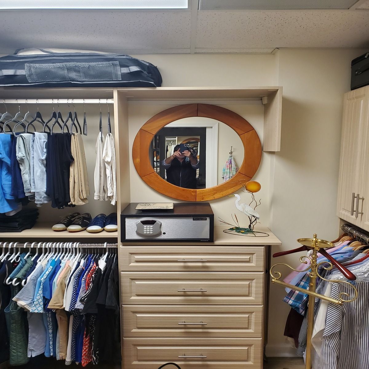 A walk-in closet with clothes racks, drawers, and a safe. A round mirror reflects the person taking the photo.