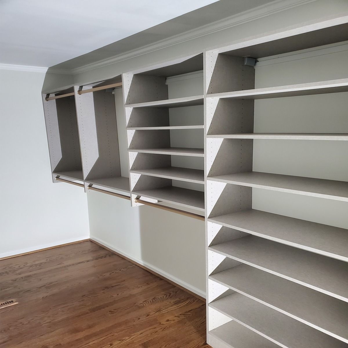 White built-in closet with shelves and hanging rods. Wooden floor.