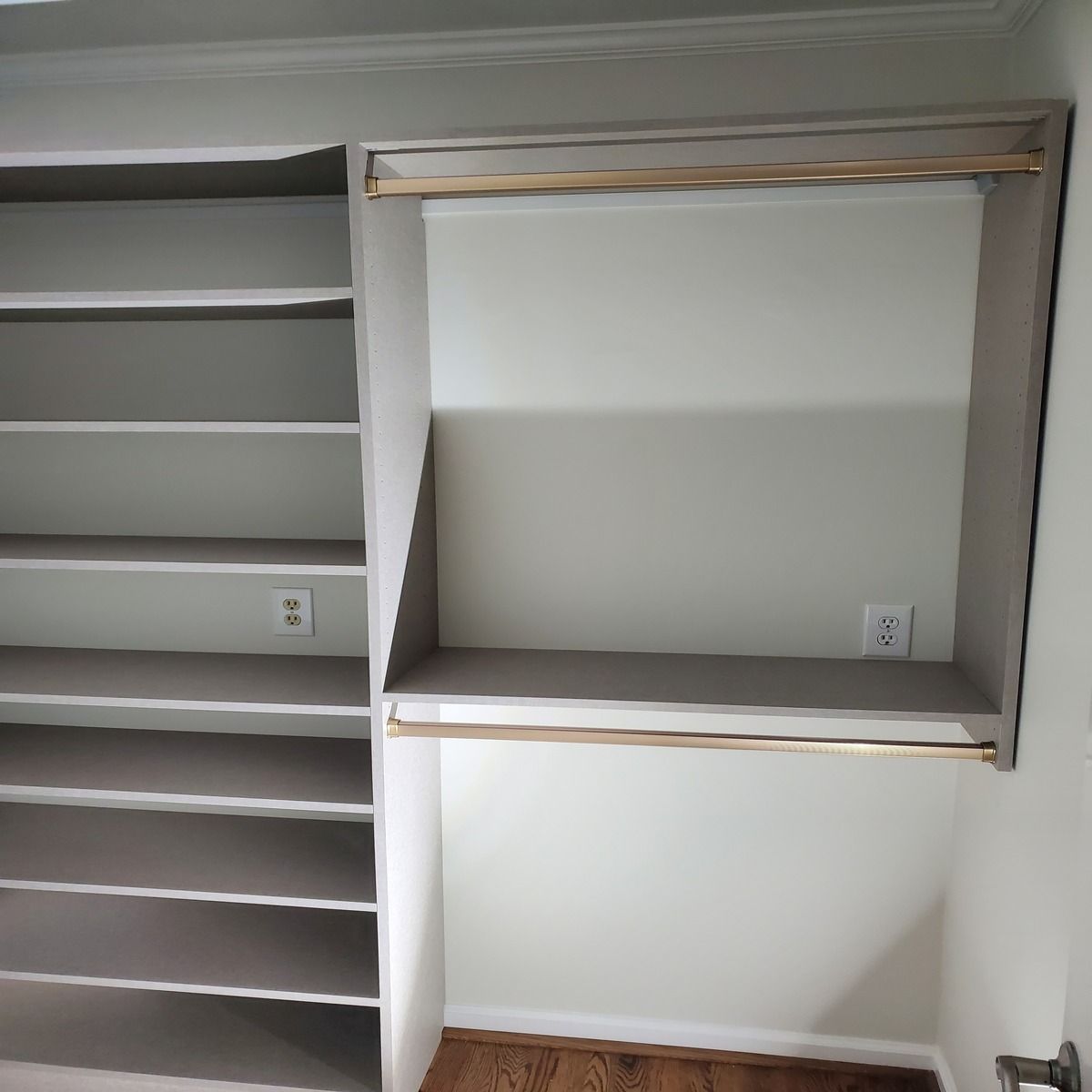 Built-in closet organizer with shelves and hanging rods, painted light grey. Two electrical outlets are visible.