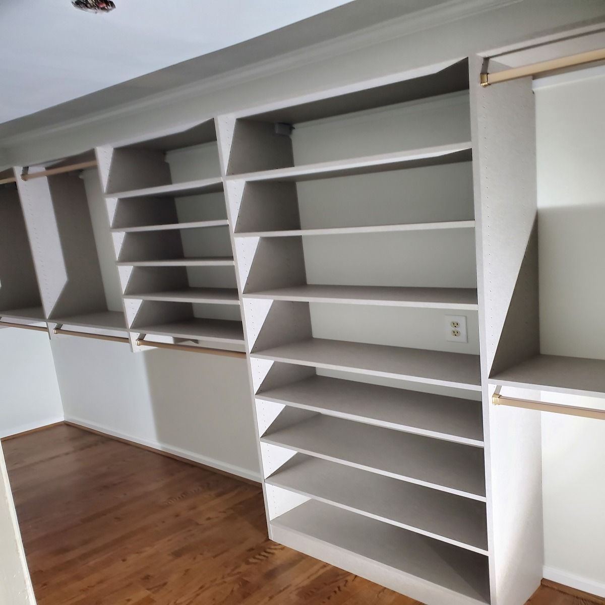 Custom built-in closet with shelves and hanging rods. The shelves are light gray, and the floor is hardwood.