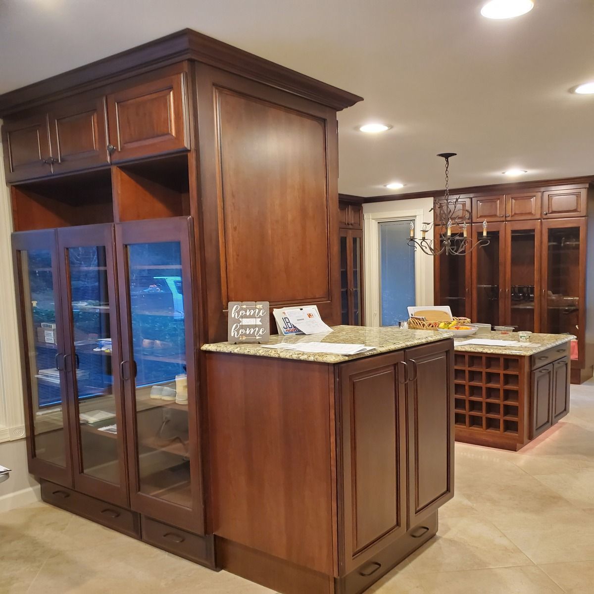 A kitchen with dark wood cabinets, including a cabinet with glass doors, granite countertops, and an island with wine storage.