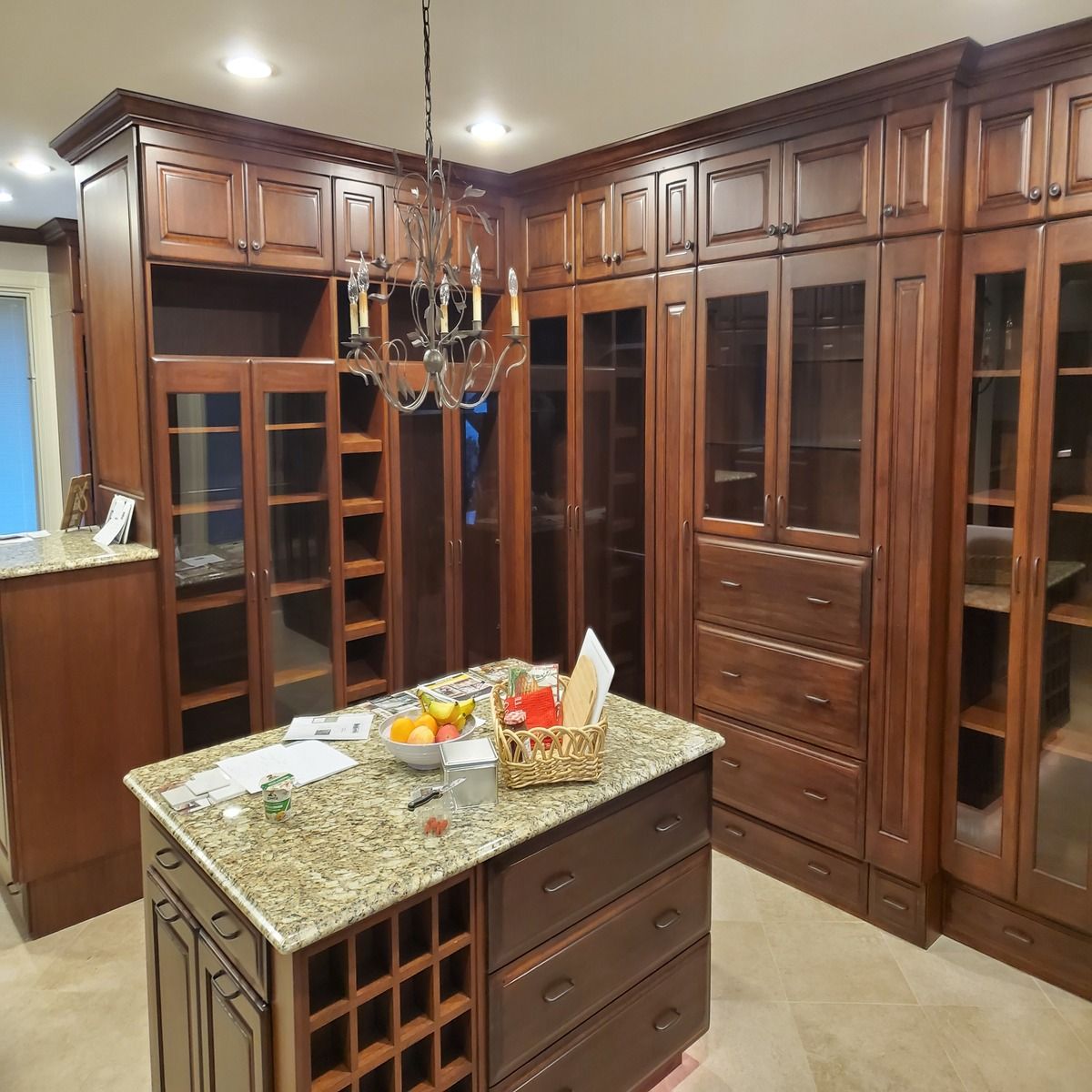 A luxury walk-in closet with dark wood cabinetry, glass doors, an island with a granite countertop, and a chandelier.