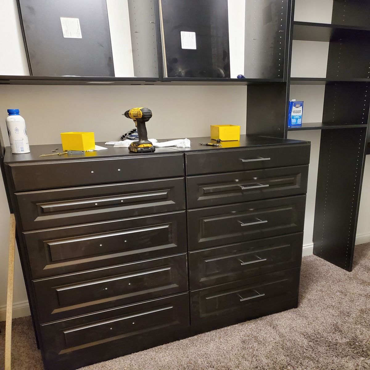 A partially assembled black dresser and shelving unit in a room. Tools and accessories sit on top.