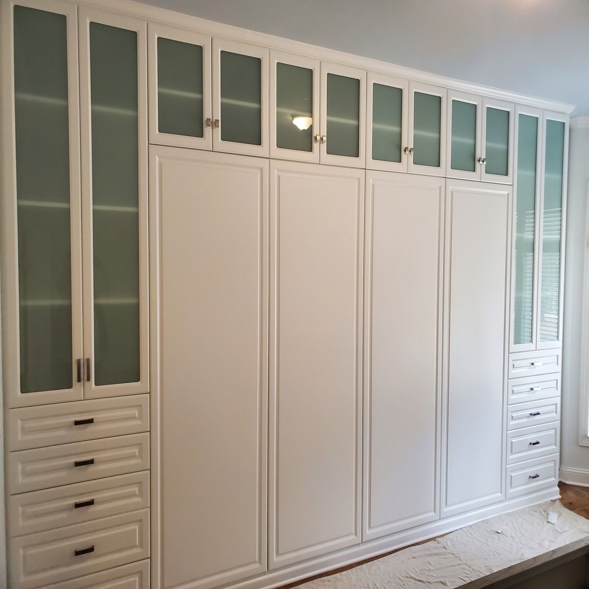 White built-in wardrobe with frosted glass upper cabinets, drawers, and a tall section.