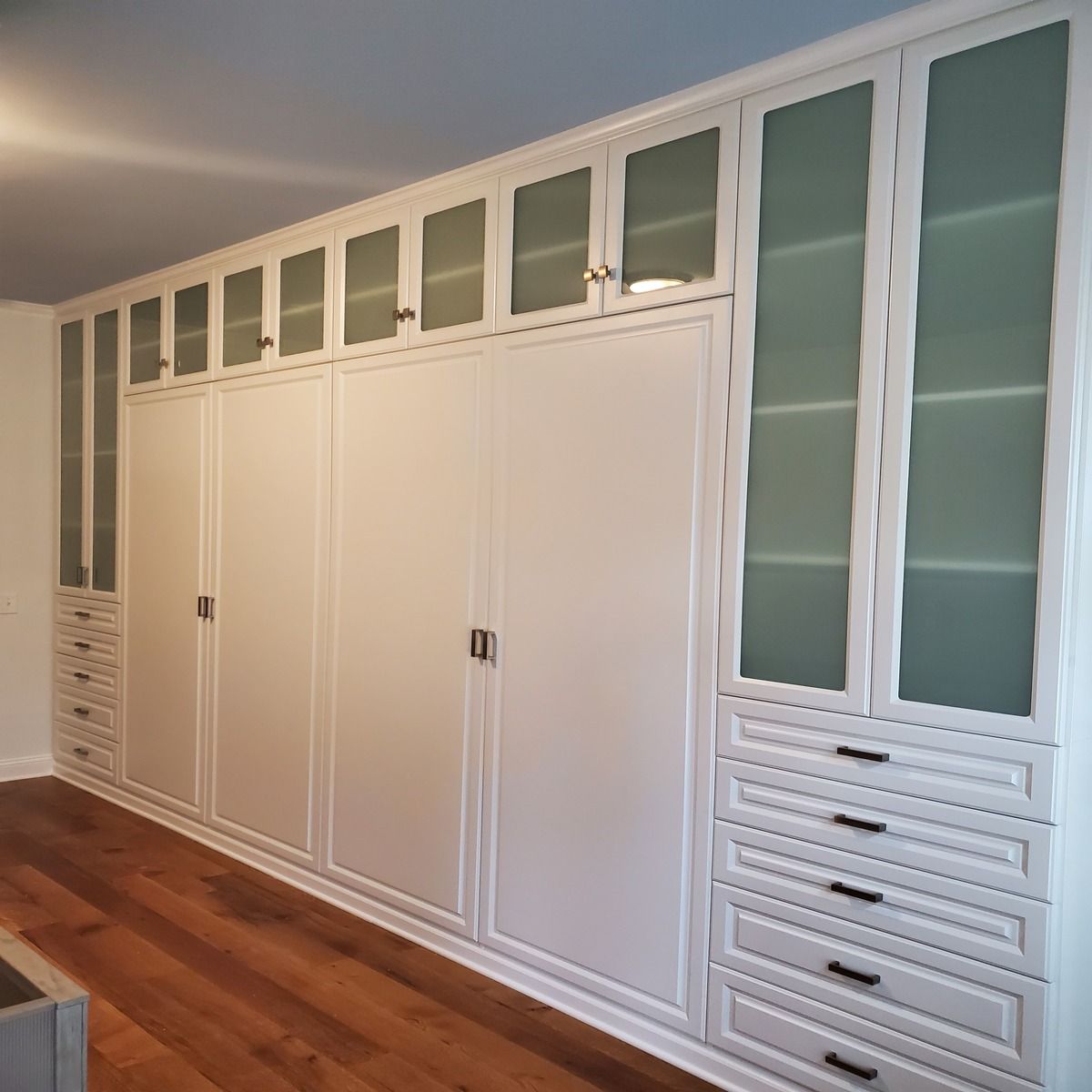 White built-in closet with solid and glass-paneled doors and drawers. Wooden floor and light-colored walls.