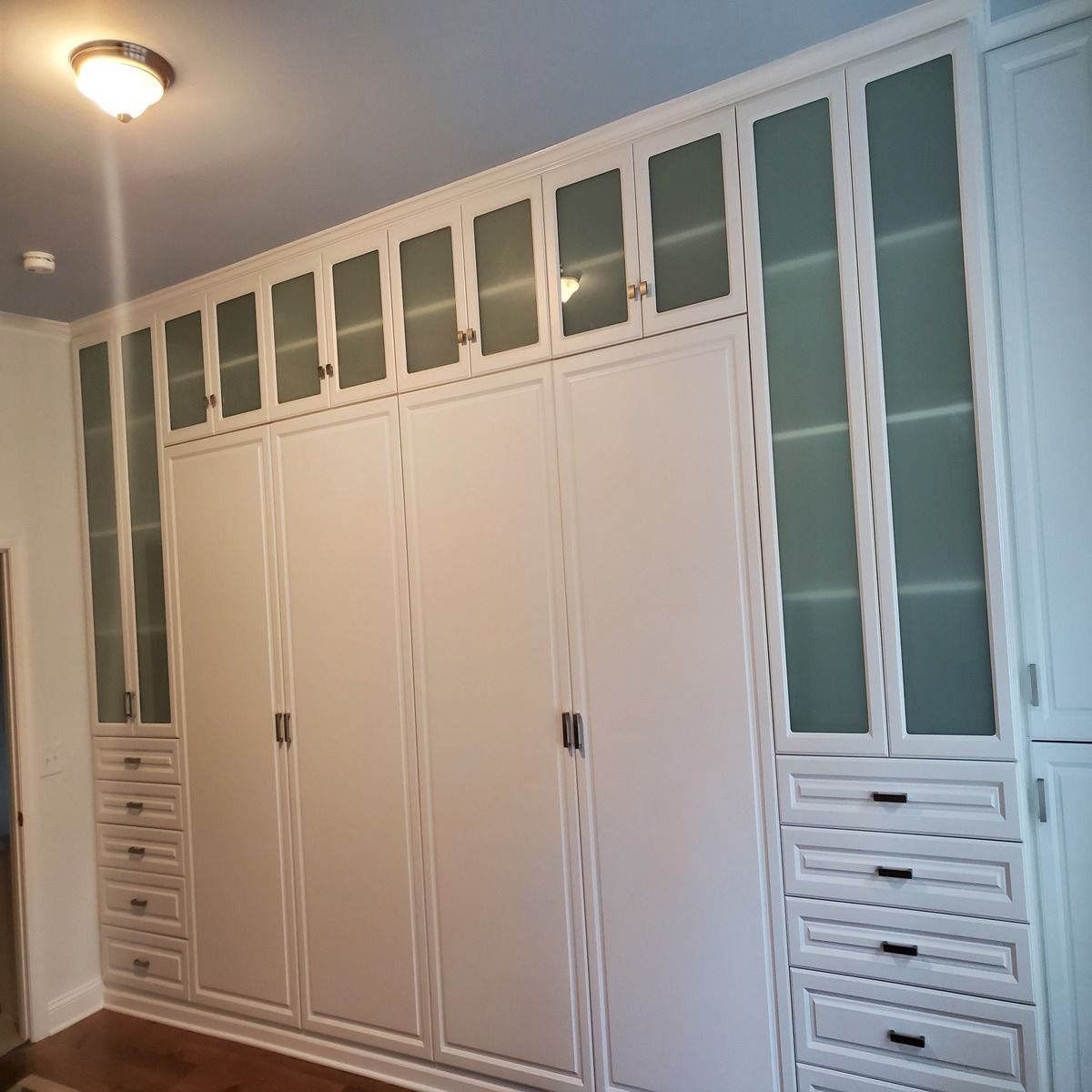 White built-in closet with multiple doors and drawers. Some doors have frosted glass panels, and the setting appears to be a bedroom.