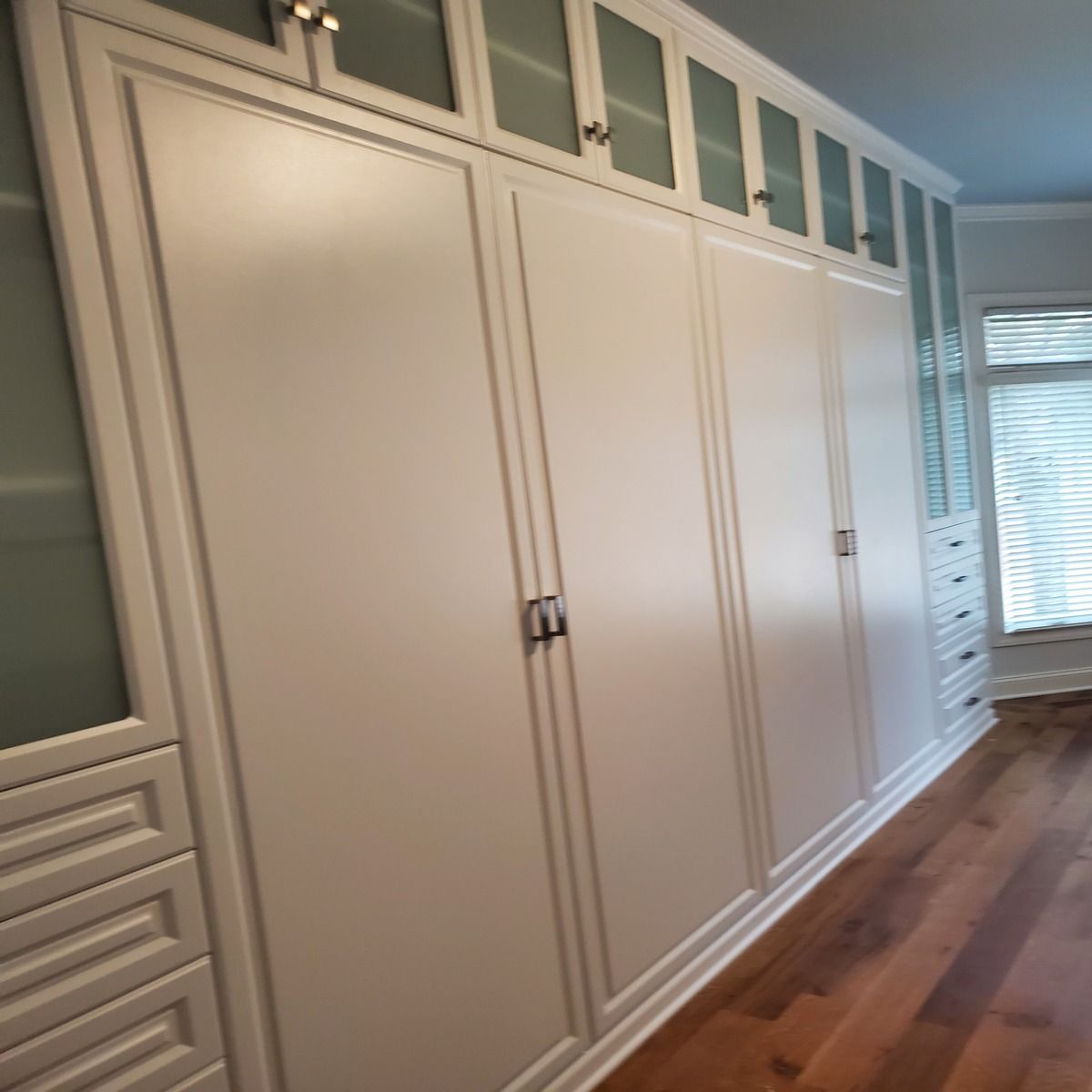 Built-in white wardrobe with multiple doors and frosted glass panels above. A tall dresser with drawers is seen to the right.