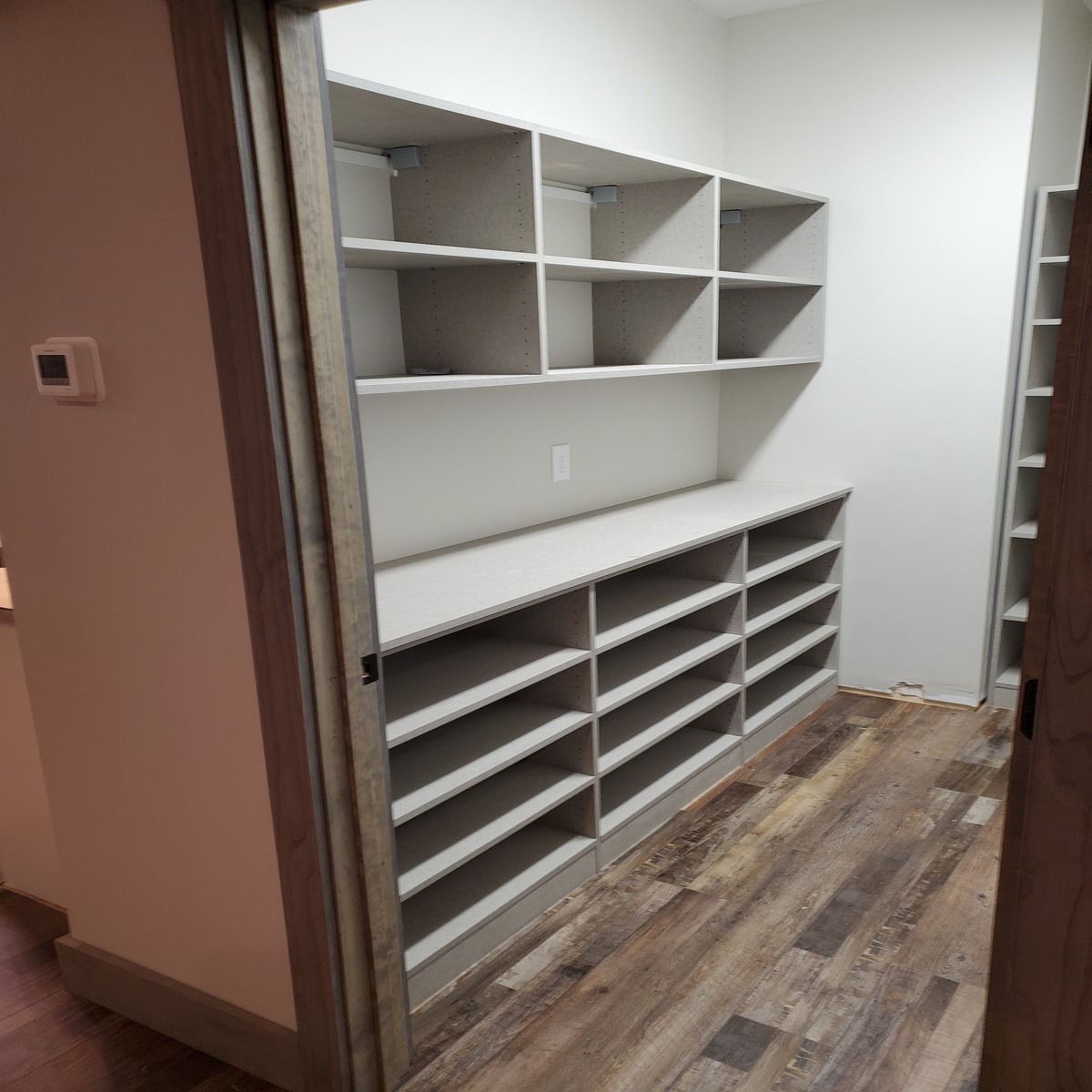 A walk-in pantry with built-in shelves and drawers painted light gray. Wood flooring completes the interior.