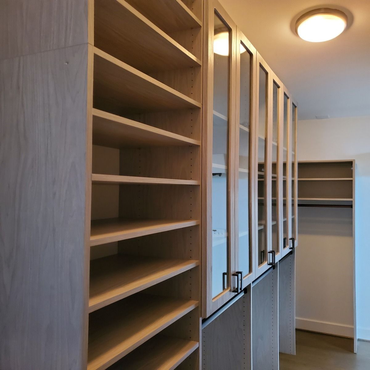 Custom closet with open shelving and glass-front cabinets in a neutral color. A matching closet is visible in the background.