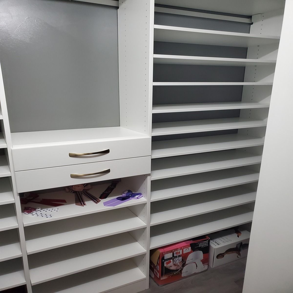 White closet shelving unit with drawers, various shelves, and a mirror on the left. Some items are on the bottom shelves.