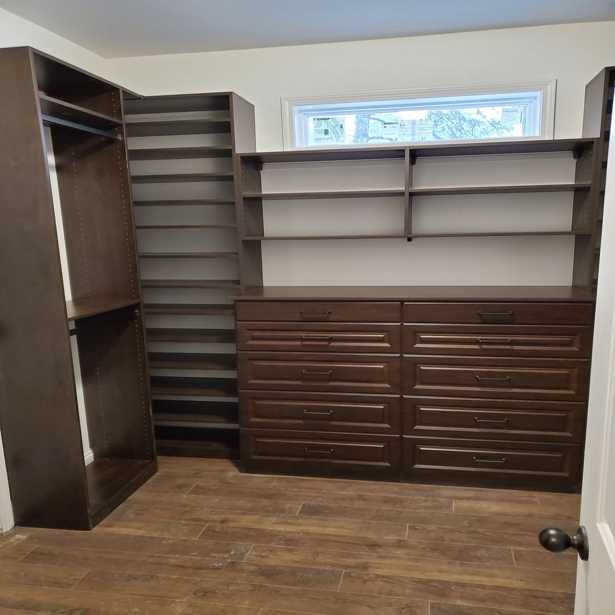 Dark brown custom closet with shelves, drawers, and a hanging rod, set against a light-colored wall.