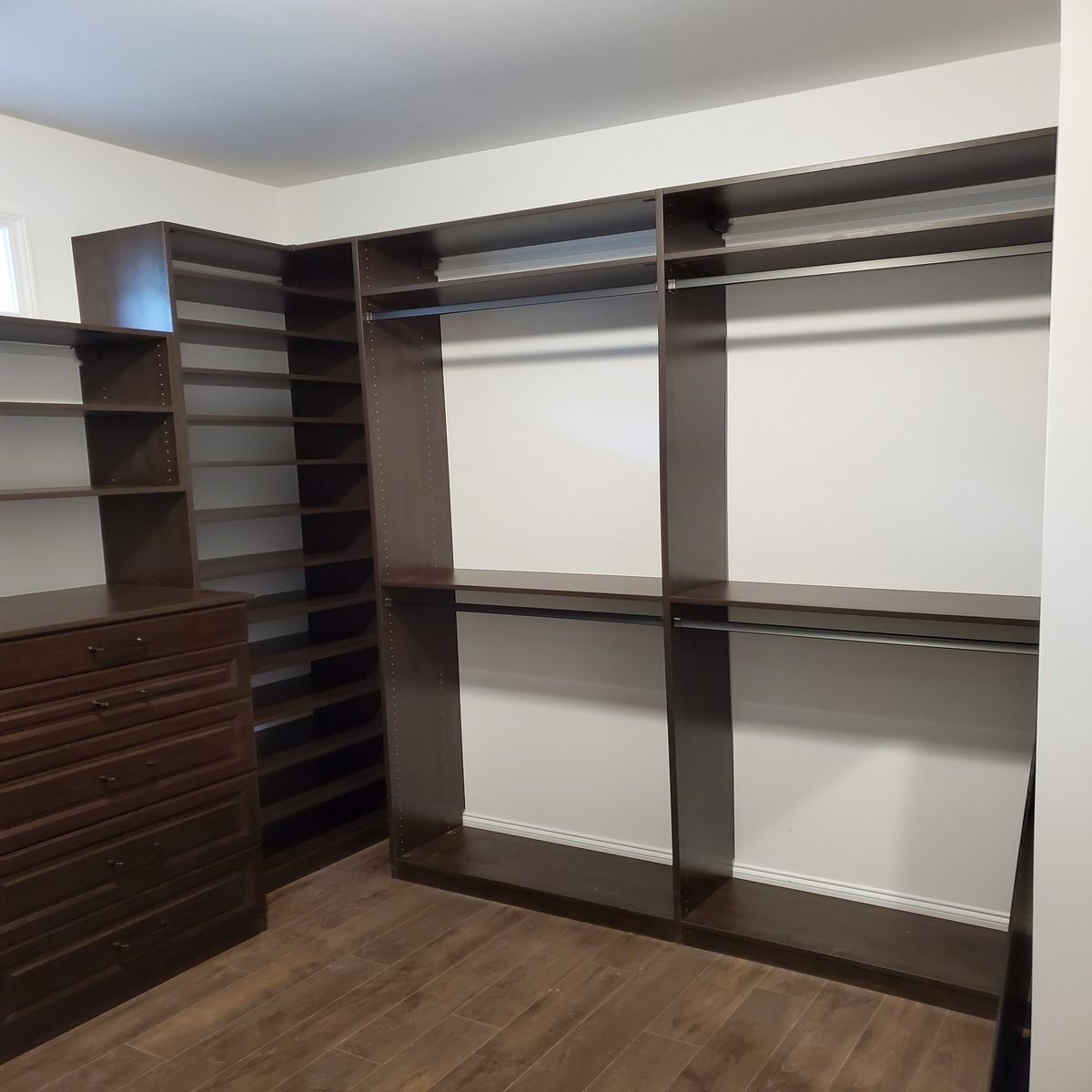 A dark brown walk-in closet with shelves, rods, and drawers. The floor is dark wood.