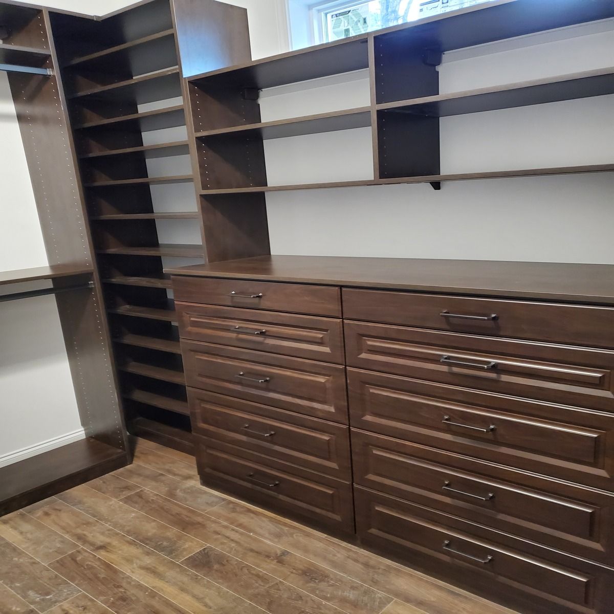 Dark brown custom closet with shelves, drawers, and a tall shoe rack. Wood flooring in a bedroom.