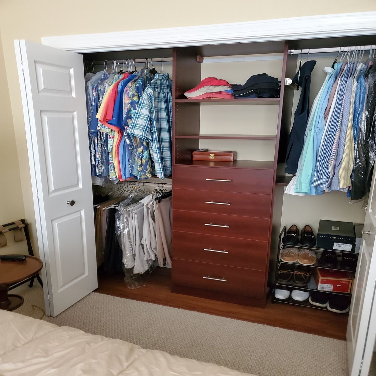 A closet organizer with hanging clothes, shelves, and drawers. Shoes are stored on the floor. The closet door is ajar.
