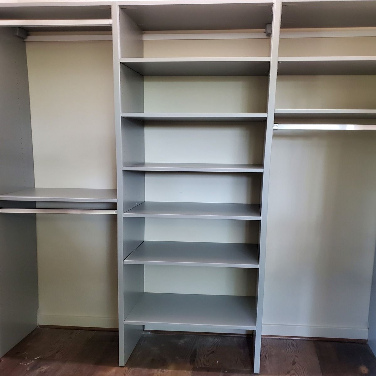 Empty built-in closet with gray shelves and rods, painted light gray. Wooden floor.