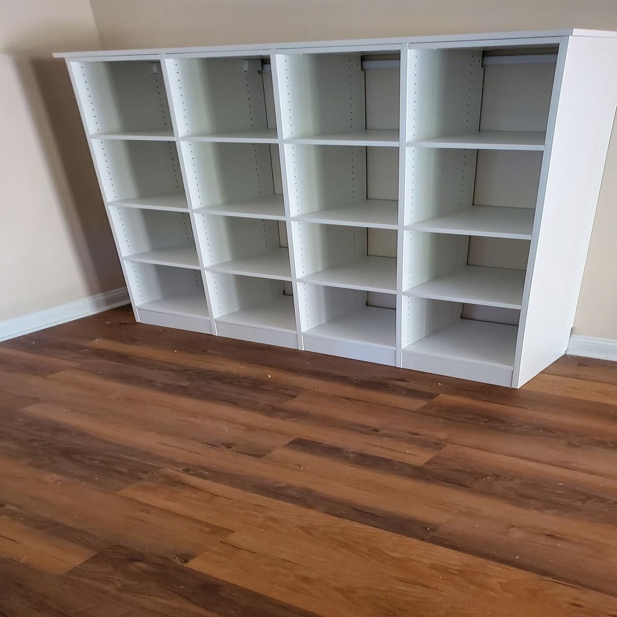 White bookshelf with 16 cubbies, against a beige wall on a wood-grain floor.