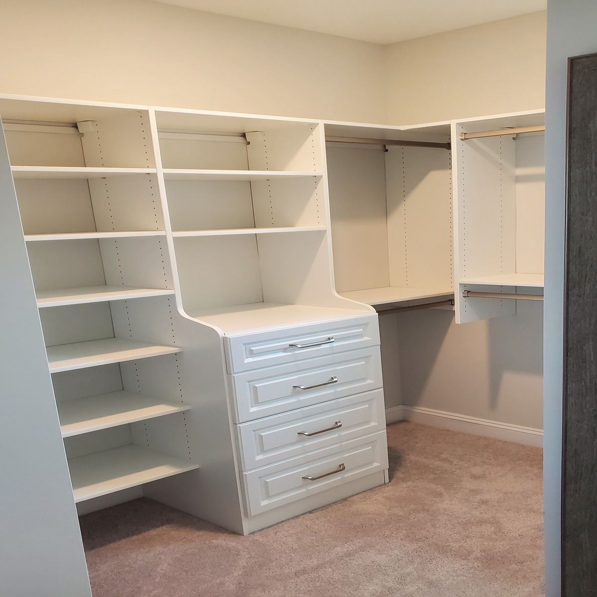 A custom-built white closet with shelves, drawers, and a clothing rod, on a pinkish carpet.