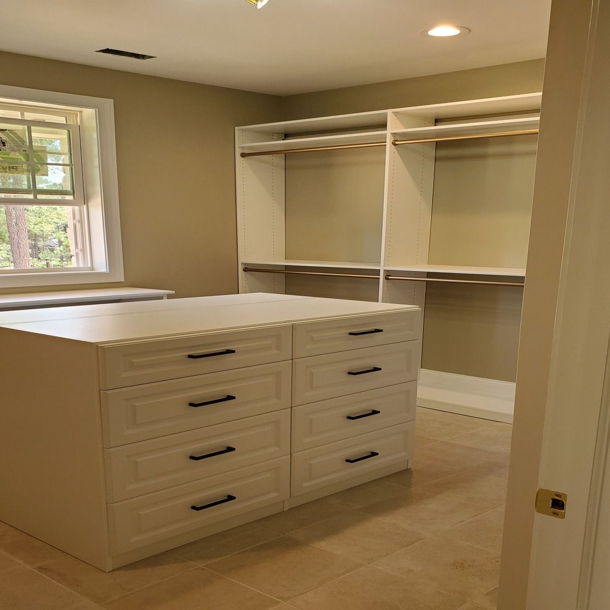 A newly renovated walk-in closet with a central island of drawers and custom shelving. The room is painted in neutral tones.
