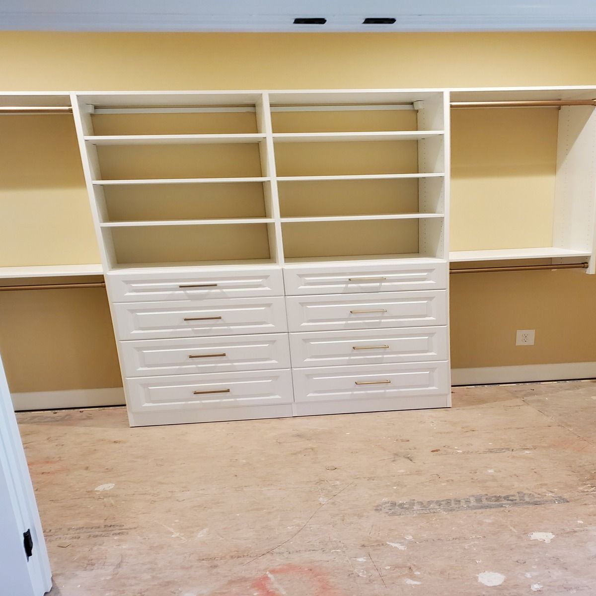 White closet shelving unit with drawers and shelves installed against a yellow wall. Beige floor is visible.